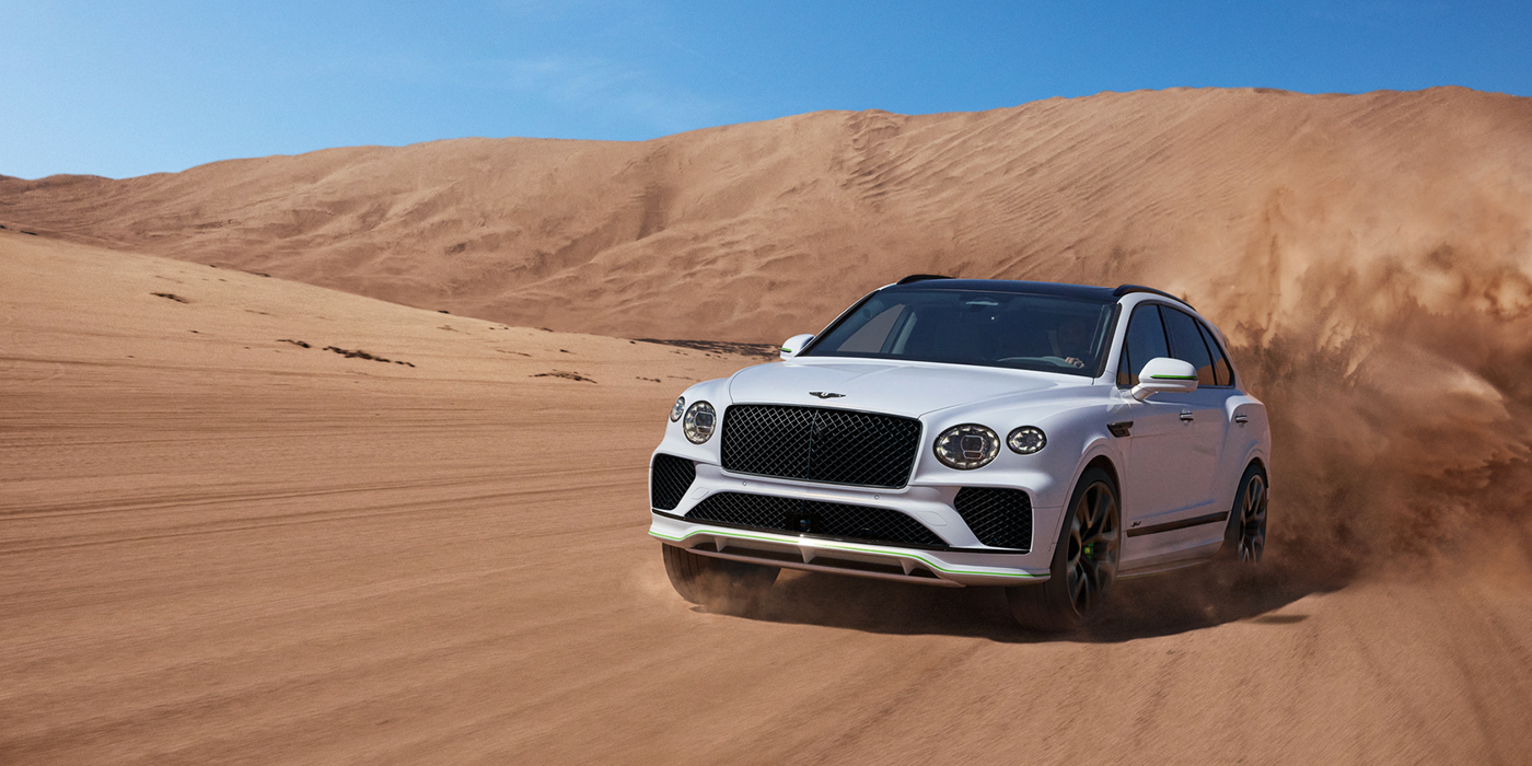 Bentley Surrey Bentley Bentayga Speed SUV front three quarter in Snow Quarts Pearlescent by Mulliner white paint driving dynamically through the desert