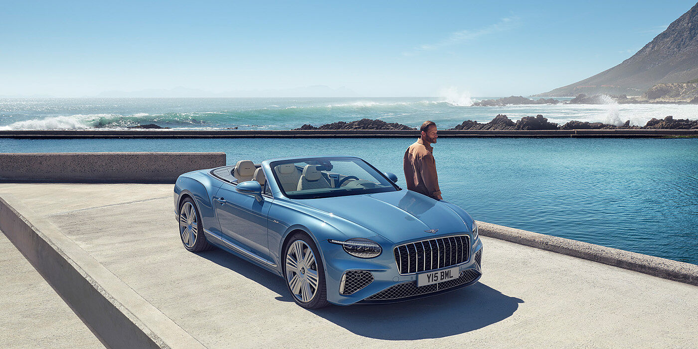 Bentley Surrey New Bentley Continental GTC Azure convertible front view in Light Windsor blue paint with 22 inch ten spoke wheels parked by the sea in the sunshine