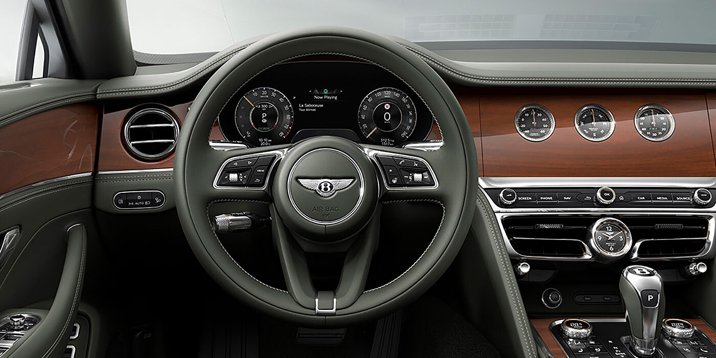 Bentley Surrey New Bentley Flying Spur sedan front cabin in Cumbrian Green hide and Crown Cut walnut veneer showing steering wheel and Rotating Display with three clocks on face