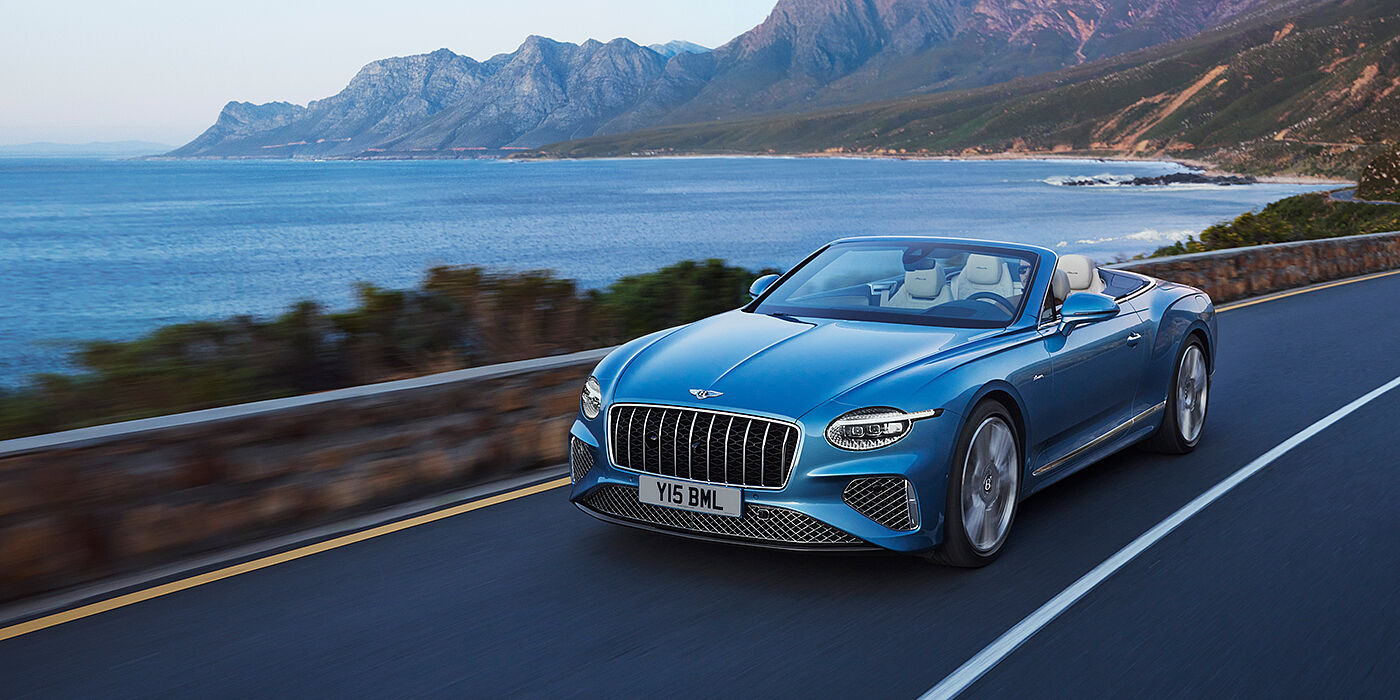 Bentley Surrey New Bentley Continental GTC Azure convertible in Light Windsor blue paint with 22 inch Azure wheels and chrome grill, driving dynamically by the sea