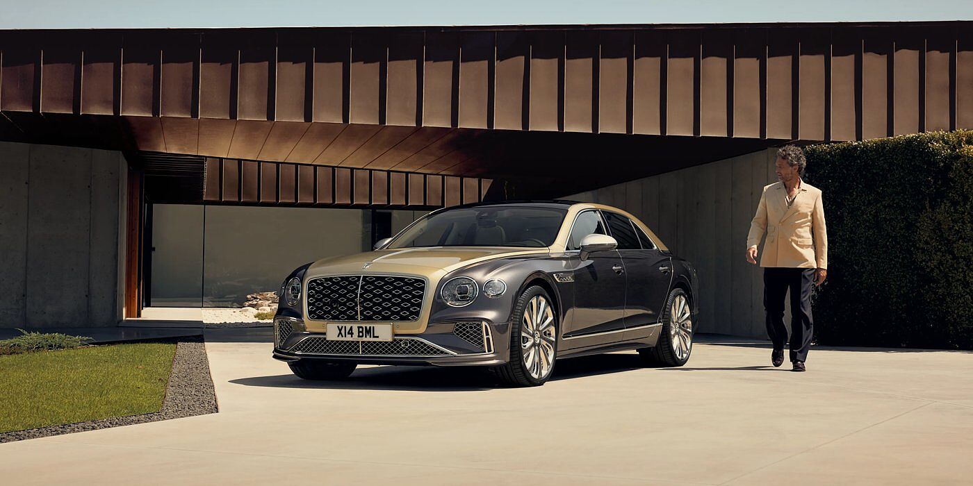 Bentley Surrey Bentley New Flying Spur Mulliner V8 hybrid sedan front three quarters in Rose Gold over Magnetic paint, parked near modern home