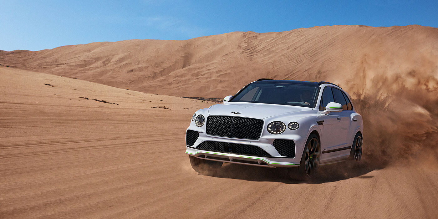 Bentley Surrey Bentley Bentayga Speed SUV front three quarter in Snow Quarts Pearlescent by Mulliner white paint driving dynamically through the desert