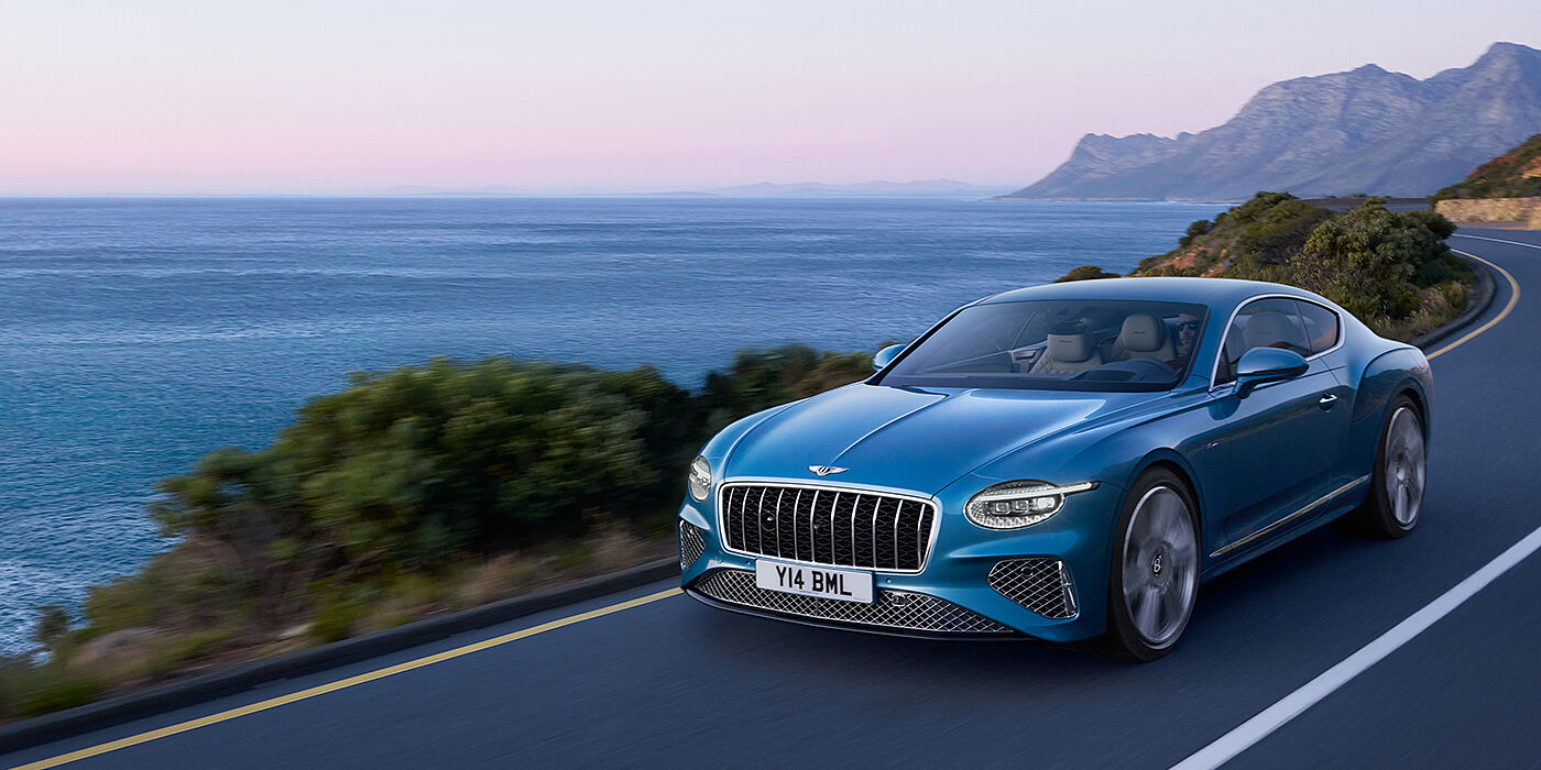 Bentley Surrey New Bentley Continental GT Azure coupe in Light Windsor blue paint with 22 inch Azure wheels and chrome grill, driving dynamically by the sea