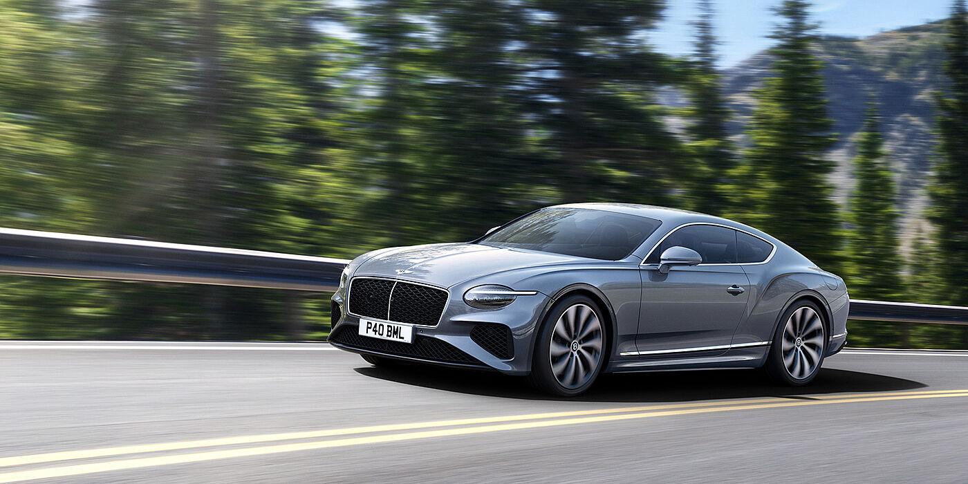 Bentley Surrey New Bentley Continental GT coupe in Silverlake paint and 22 inch ten-spoke wheels, driving dynamically on a tree-lined road in the sunshine