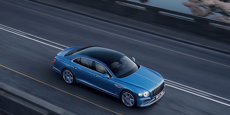 Bentley Surrey New Bentley Flying Spur Azure sedan in Light windsor blue paint by Mulliner, with 22 inch Azure wheels seen from overhead driving dynamically on a country road