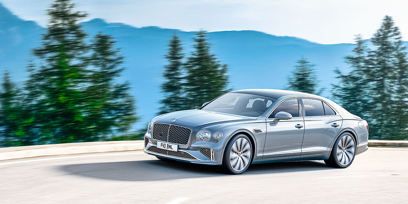 Bentley Surrey New Bentley Flying Spur sedan side view in Silverlake paint with ten spoke wheels and chrome matrix grille driving dynamically on a mountain road