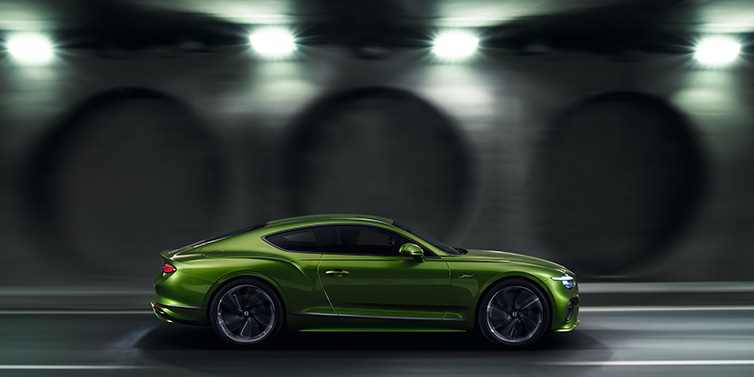 Bentley Surrey Bentley Continental GT Speed coupe profile in Tourmaline Green driving dynamically past a concrete wall at night