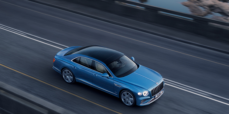 Bentley Surrey New Bentley Flying Spur Azure sedan in Light windsor blue paint by Mulliner, with 22 inch Azure wheels seen from overhead driving dynamically on a country road