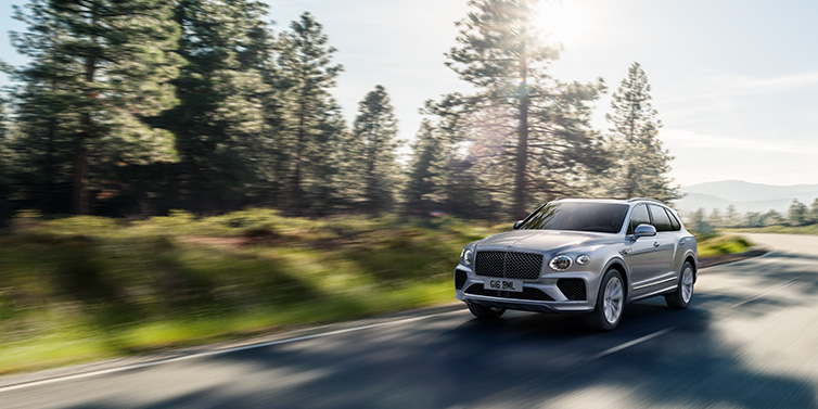 Bentley Surrey Bentley Bentayga SUV front three quarter in Moonbeam silver paint driving dynamically along a tree-lined road