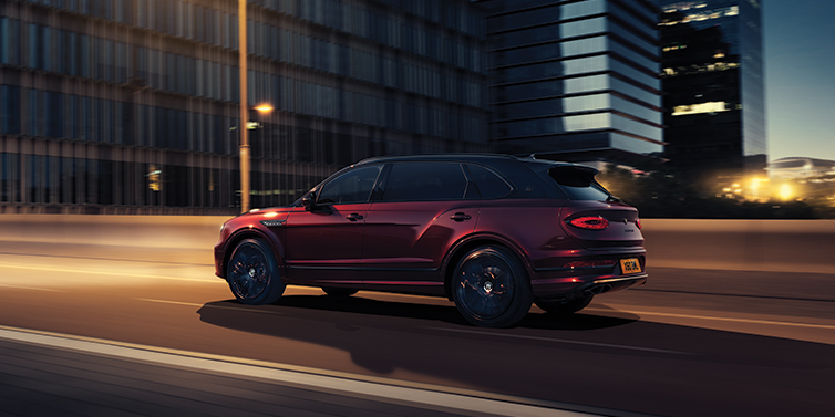 Bentley Surrey Bentley Bentayga Extended Wheelbase Mulliner SUV in Cricket Ball red paint driving dynamically in city at night