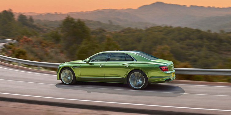 Bentley Surrey Bentley Flying Spur Speed sedan side profile in Tourmaline Green paint driving dynamically on a mountain road at sunset